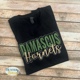 A close up photo of a black cotton crew neck t-shirt with a Damascus Hornets logo in dark green and gold glitter surrounded by AB rhinestones. 