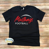 A black short-sleeve t-shirt with a 'Mustangs Football' graphic printed on the front, laid flat on a rustic wooden plank background. The graphic features 'Mustangs' in red script, 'FOOTBALL' in white block letters, and a white football graphic arching above the text.